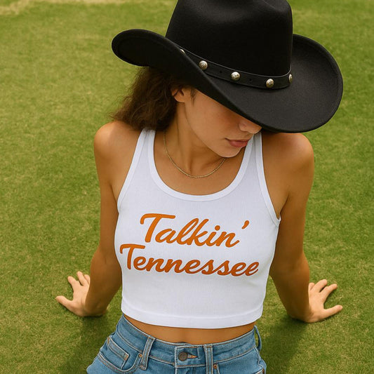 Person wearing a white tank top with 'Talkin' Tennessee' text, denim shorts, and red boots on grass.